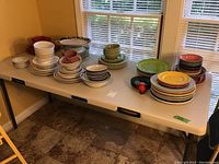 Overview of multiple stacks of dishes and bowls arranged on a white table near a window. Items are grouped by color and size.