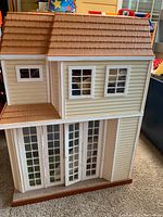 Front exterior of the light beige plastic doll house with brown shingled roof and white window frames