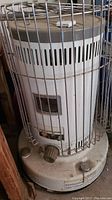 Front angled view of Toyoset Omni 230 kerosene heater with protective cage showing its cylindrical white body, vents, and control knobs.