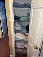 Closet shelving filled with stacked folded linens, towels, and a blanket at the bottom.