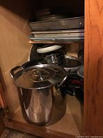Stainless steel large stock pot with lid and various metal baking sheets in kitchen cabinet