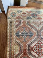 Close-up of the rug corner showing the detailed geometric and border pattern with colors of cream, rust, blue, and brown.