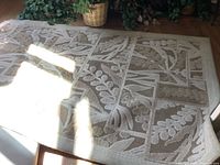 Photo of beige area rug with leaf patterned design, sunlight casts shadow on rug surface, showing texture and design details.