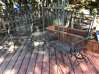 Full view of the outdoor round metal table with two metal rocking chairs on a wooden deck, showing overall set and outdoor environment.