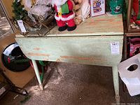 Front view of wooden green drop leaf table with chipped paint and folding sides down, showing wear and paint loss.