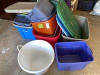 Overall view of stacked assorted colored plastic storage totes and lids on garage floor.