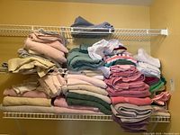 Wide view of multiple stacks of folded bath towels, hand towels, and washcloths arranged on wire shelving