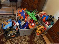 Four large plastic totes filled with various toys including Nerf guns, a dollhouse, and toy vehicles. Scooby-Doo bag visible.