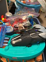 Photo showing a black and gray futuristic toy vehicle or spaceship placed on a teal plastic base with other small toys packed in bags and containers