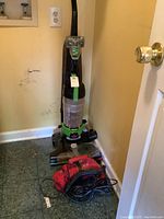 Bissell Powerforce Helix Turbo Rewind upright vacuum alongside Dirt Devil red hand vacuum on floor near laundry area.