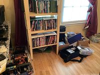Shelf with multiple rows of DVDs and VHS tapes, boxes and totes on the floor containing more media items.