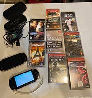 Full lot with two PSP consoles, 9 game cases with visible titles, charger, carrying case, and wrist strap.
