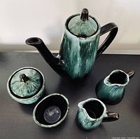 Five-piece Blue Mountain Pottery coffee service on black surface, green and black glaze, includes coffee pot, sugar bowl, creamer, small pitcher, small bowl