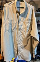 Full view of light beige long sleeve fishing shirt with multiple pockets on front hanging on hanger