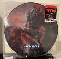 Front side of the Dio Angy Machines picture disc vinyl record featuring artwork of a robotic figure in a dystopian setting with logo and sticker.