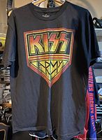 Front view of large black T-shirt featuring a Kiss Army logo with a yellow and red shield design.