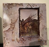 Front cover image of Led Zeppelin vinyl record featuring textured wallpaper with peeling sections and framed photo of man carrying sticks.