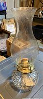 Glass oil lamp with ribbed base and tall chimney shown from side angle to display lamp structure and condition.