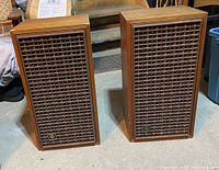Pair of Rectilinear wooden loudspeakers with lattice grills in upright position on floor.