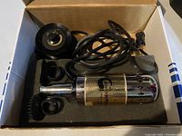 Sonoid massage device with power cord and attachments inside open box with foam casing.