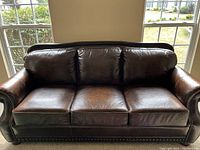 Front view of brown leather three-seat couch showing cushions, rolled arms, nailhead trim