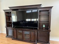 Front view of large wooden entertainment center with dark finish, holding a large flat screen TV and displaying shelving and cabinet compartments.