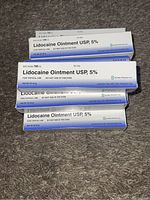 Top view shows multiple stacked boxes of Lidocaine Ointment USP 5% displaying brand name, concentration, and instructions.
