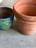 Two large pottery plant pots side by side, showing a plain terracotta pot and a painted ceramic pot with floral designs.