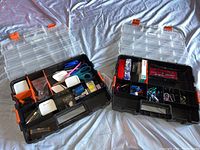 Two open plastic and orange latches stackable toolboxes showing various office items inside such as scissors, staplers, and pencil sharpeners