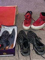 Three pairs of men's shoes, including a red pair of Nike Air Jordans and two pairs of black athletic shoes, one in a box and one on the floor.