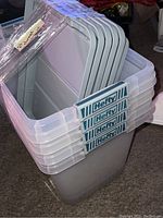 Side view showing stack of four clear plastic Hefty storage containers with grey locking lids on top, brand labels attached.