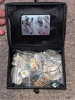 Open jewelry box showing assorted jewelry in small plastic bags inside, mirror on lid visible.