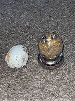 Two small egg-shaped decorative objects; one clear resin sphere with gold flakes and silver skulls on a silver stand, and one rough white object potentially a stand or decorative element.