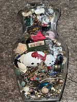 Glass jar filled with a dense assortment of jewelry viewed from an angle showing many colorful beads and brooches.