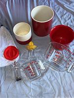 Pyrex glass measuring cups, juicer, pepper grinder, kitchen pots, and cloth bags arranged on fabric surface