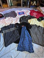Overhead view of clothing items spread on floor including T-shirts, caps, and sleeveless shirts.