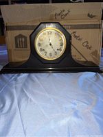 Front view of the black wooden antique mantel clock with octagonal clock face bezel and gold-tone trim.