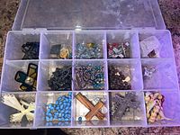 Top view of plastic jewelry box with multiple compartments filled with assorted religious jewelry including crosses and rosaries.