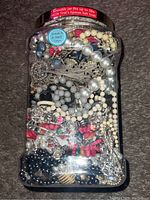 View of the plastic jar packed with assorted pearl necklaces, metallic bracelets, earrings, and mineral rocks.