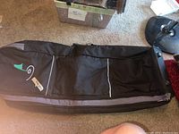 Full length view of the golf bag showing black fabric with white piping and a green/white embroidered logo, showing the zippered pockets.
