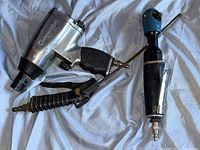 Three pneumatic ratchet wrenches laid out on a blue sheet, showing various angles and grips.