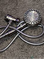 Photo of a silver handheld shower head with multiple spray nozzles, flexible metal hose, and wall mount bracket on a carpeted surface.