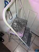 White metal 3-step ladder shown from top angle, displaying textured, non-slip aluminum steps and white frame with some signs of use.