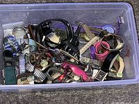 Plastic bin containing a large number of assorted watches with different colored bands and watch faces.