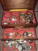 Open triple-layer cedar jewelry box showing a variety of jewelry pieces in compartments on all three levels.