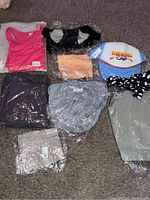 All brand new women's activewear items laid out on carpet, showing various colors and types including tank top, sports bras, yoga pants, and hat.