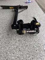 Compact black Thule bike rack with clamp attachments lying on a speckled floor.