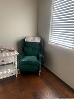 Single green recliner chair with cushioned back and wooden legs next to a white side table.
