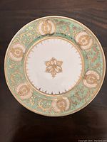 Front view of hand painted vintage porcelain dish with pale green and gold decorative border and gold center motif.