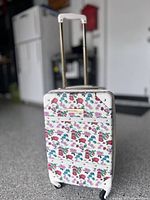 Front view of carry-on luggage with white body and multicolor floral pattern, extendable handle, and wheels.